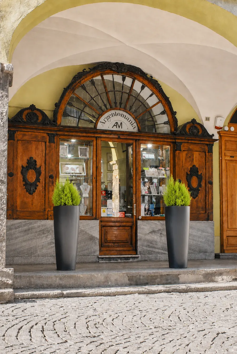 Ingresso della gioielleria Argentomania nel Palazzo Galouppe a Pinerolo: portone in legno antico con decorazioni in ferro battuto, sotto i portici del centro storico pinerolese